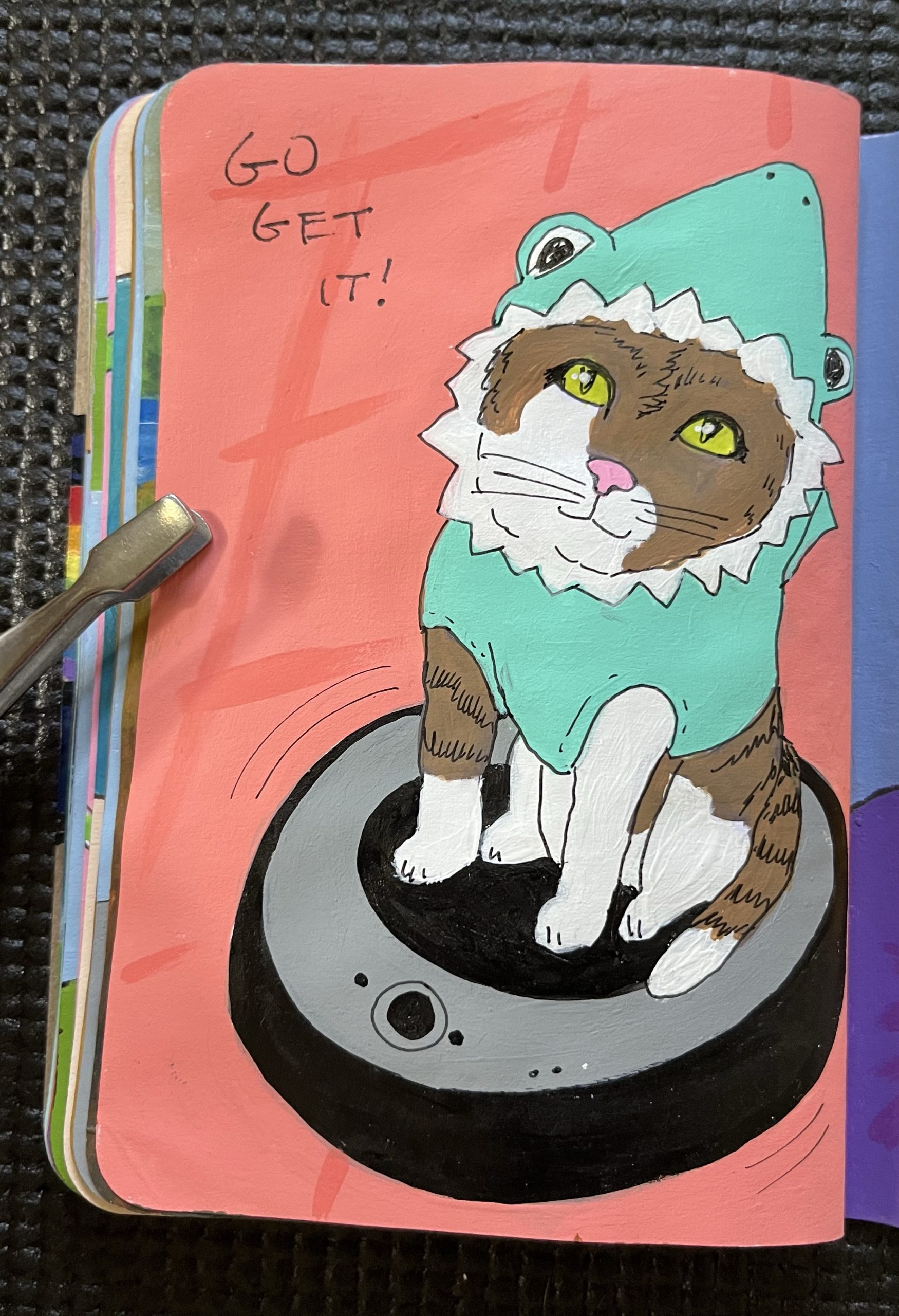 A painted page of a Kitten dressed as a shark riding a Roomba